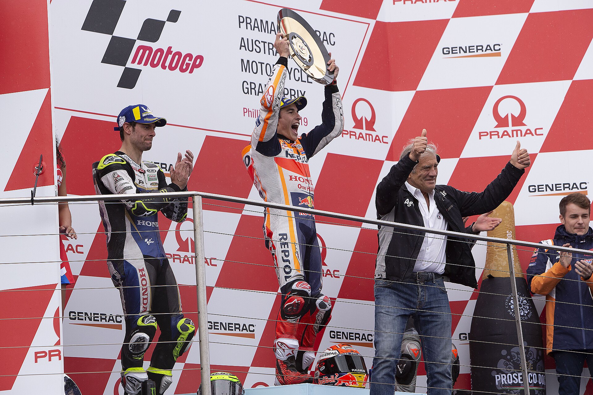 Cal Crutchlow and Marc Márquez, holding his trophy and celebrating on the podium after finishing second and first at the 2019 Australian Grand Prix.