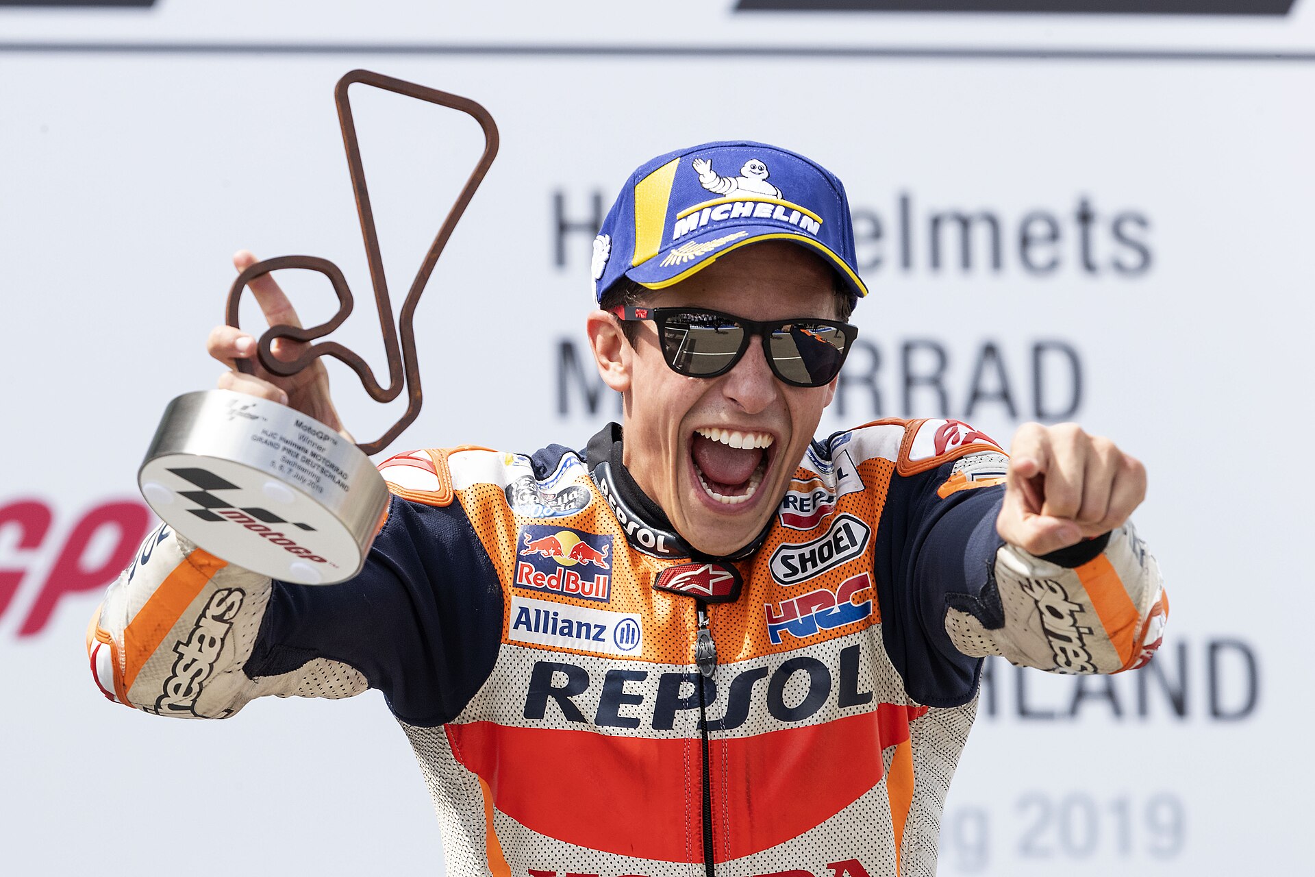 Marc Márquez, holding his trophy and celebrating on the podium after winning the 2019 German Grand Prix.